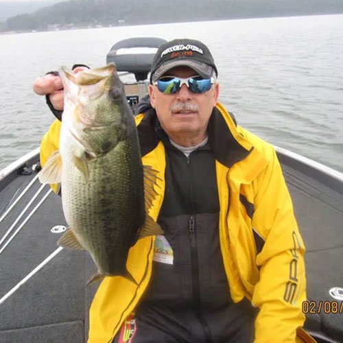 A man in a yellow jacket holds a large fish on a boat in a lake.